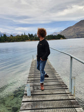 Load image into Gallery viewer, Maru wearing organic cotton long sleeve black top with gold eco friendly ink printed on front and back at Lake Wakatipu Queenstown. Maru wears a size XL
