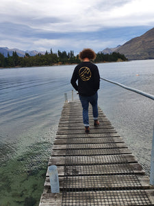 Maru wearing organic cotton long sleeve black top with gold eco friendly ink printed on front and back at Lake Wakatipu Queenstown. Maru wears a size XL