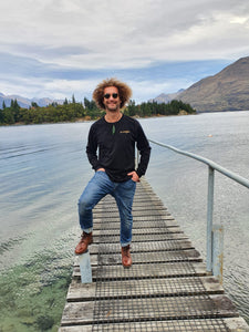 Maru wearing organic cotton long sleeve black top with gold eco friendly ink printed on front and back at Lake Wakatipu Queenstown. Maru wears a size XL