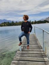 Load image into Gallery viewer, Maru wearing organic cotton long sleeve black top with gold eco friendly ink printed on front and back at Lake Wakatipu Queenstown. Maru wears a size XL
